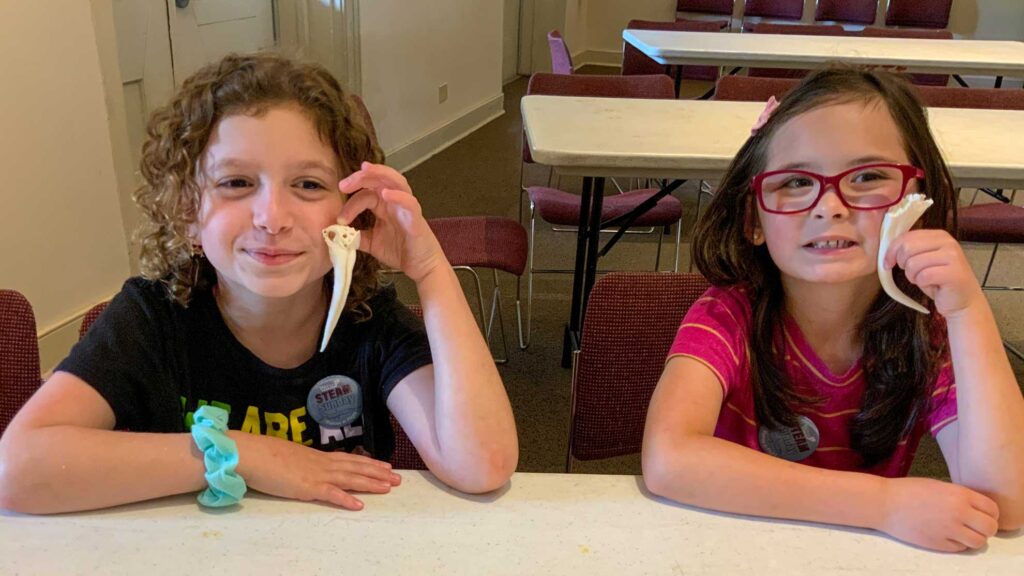 Two children holding up fangs they made at an education activity.