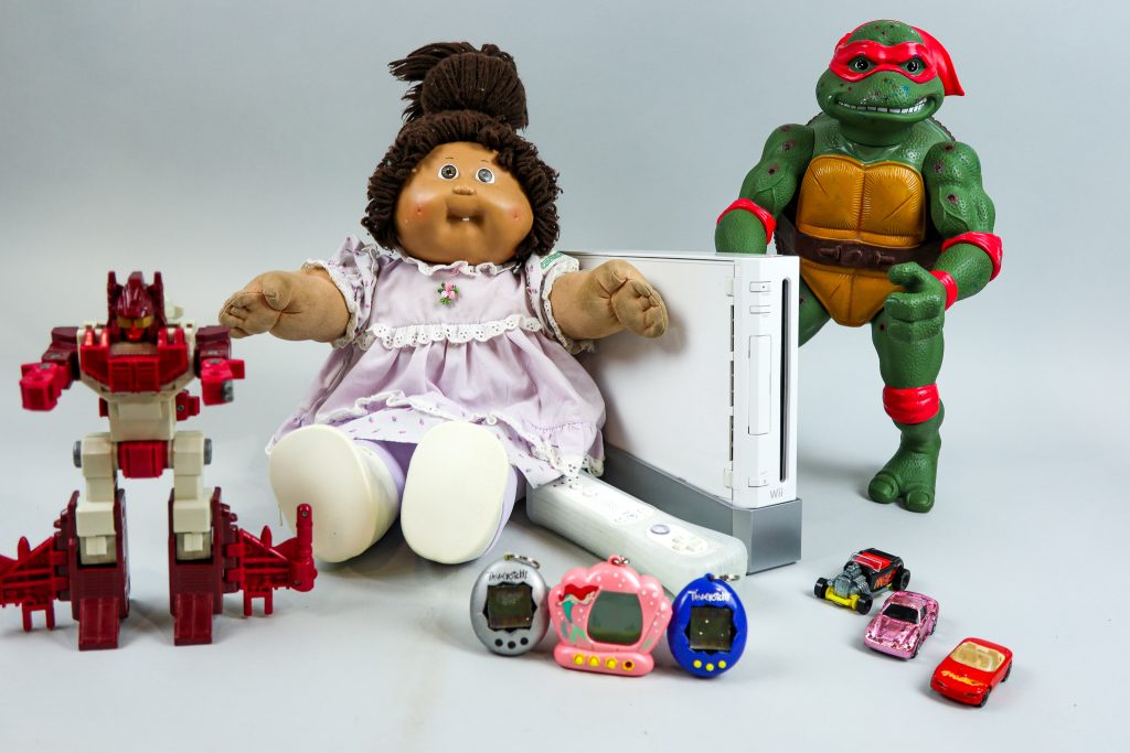 modern nostalgia toys with red transformer, cabbage patch doll, nintedo wii console, TMNT Raphael, hot wheels cars and three tamagotchi.