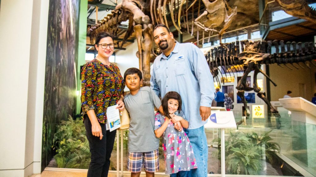 Family of four in the dinosaur gallery. Two little kids, mom and dad.