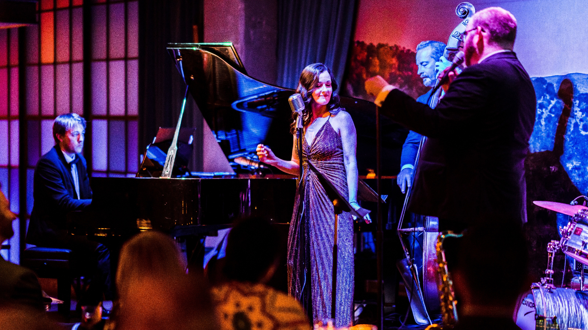 Pianist with two vocalist and one instrumentalist on stage under purple and red lights.