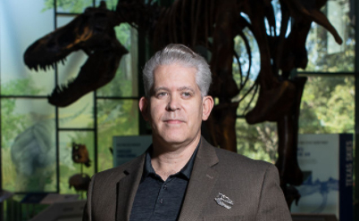 Headshot of Dr. Adams in front of the t. rex.