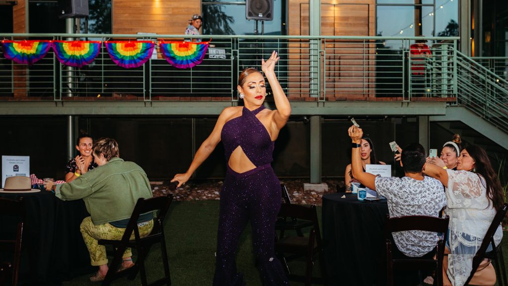 Drag queen in purple outfit, performing at a pride event.