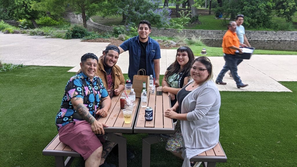 group of 5 people, casually dressed, sipping cocktails at a picnic bench.