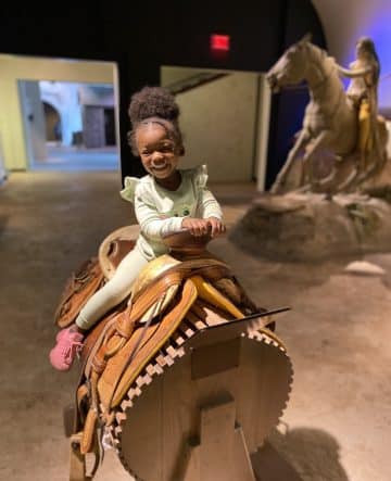 young girl smiles while sitting on a saddle.