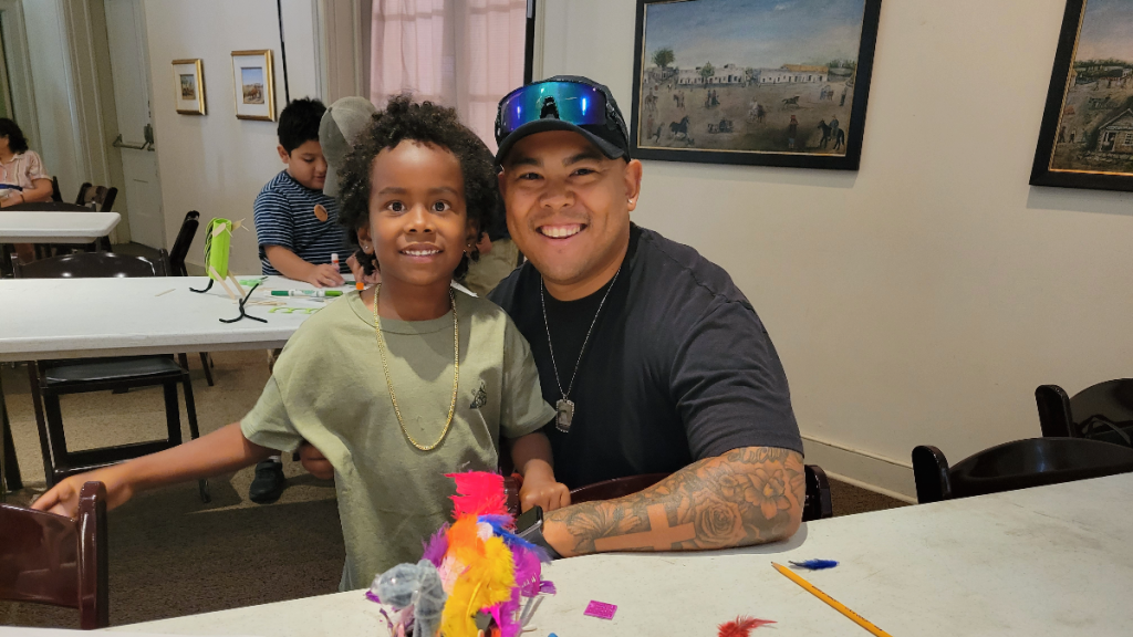Father and son smile behind a craft table.