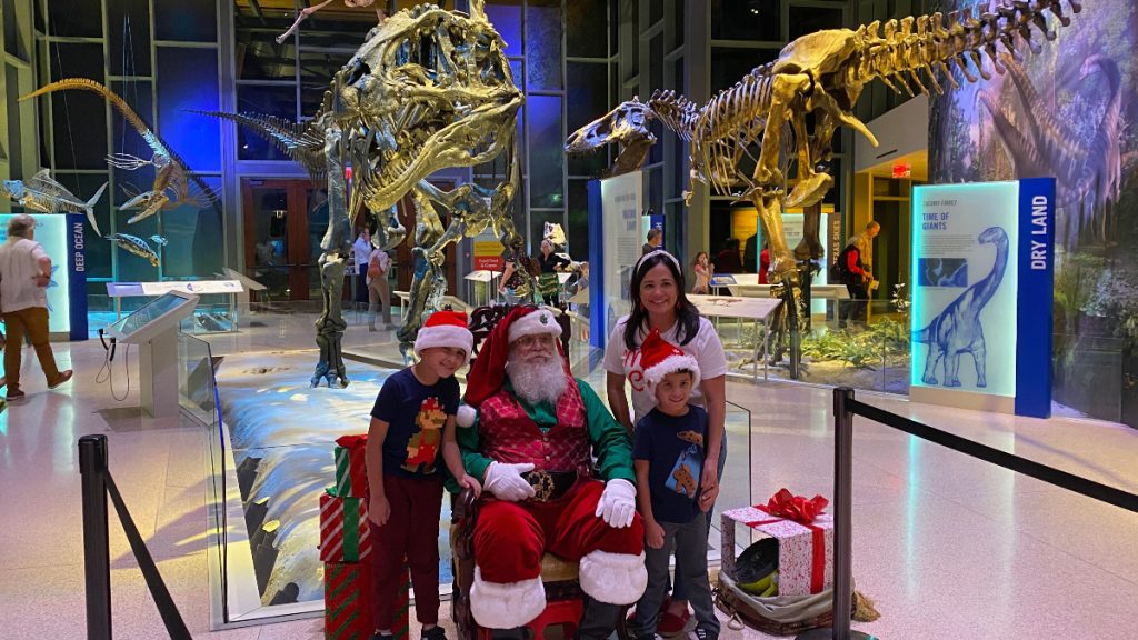 family smiles while posing with Santa and the dinosaurs