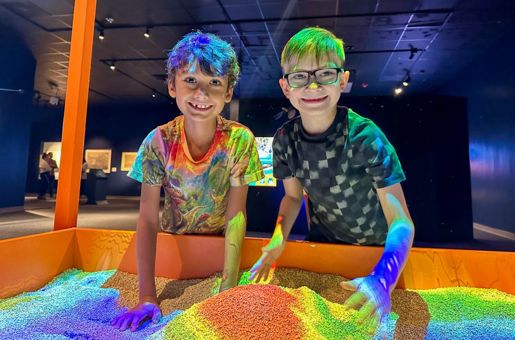 two boys smile while playing with an AR topographical map.