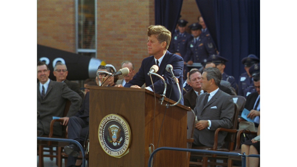 President John F. Kennedy stands behind a lectern.