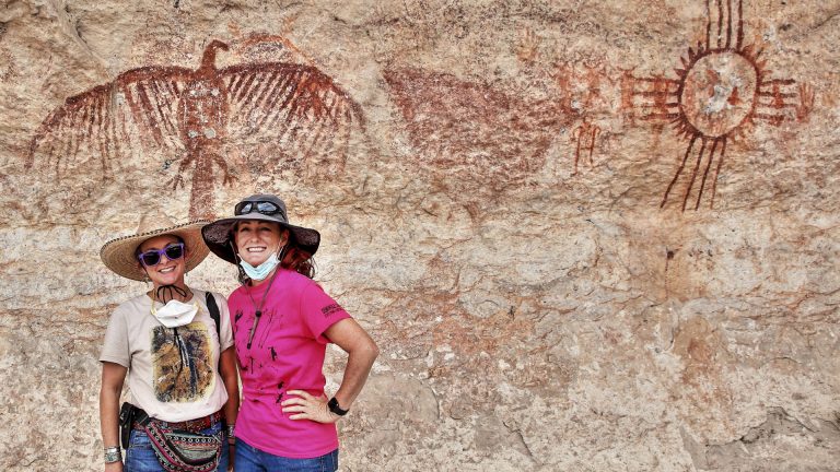 two hikers pose in front of rock art.