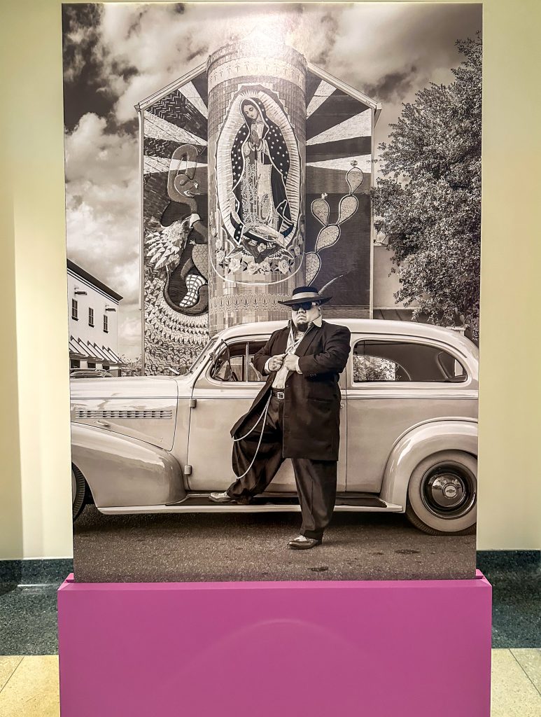 man standing in front of a car parked in front of la Virgen de Guadalupe.