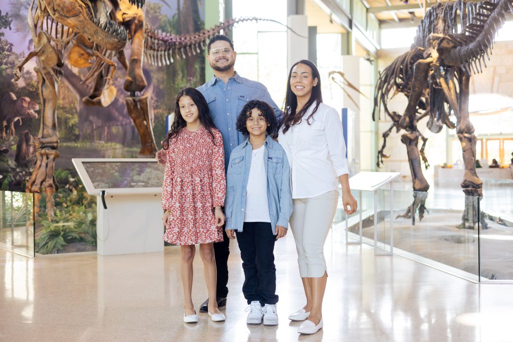 family of four smiles in the dinosaur gallery.