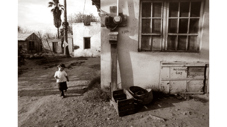 Child runs on dirt path outside a house.