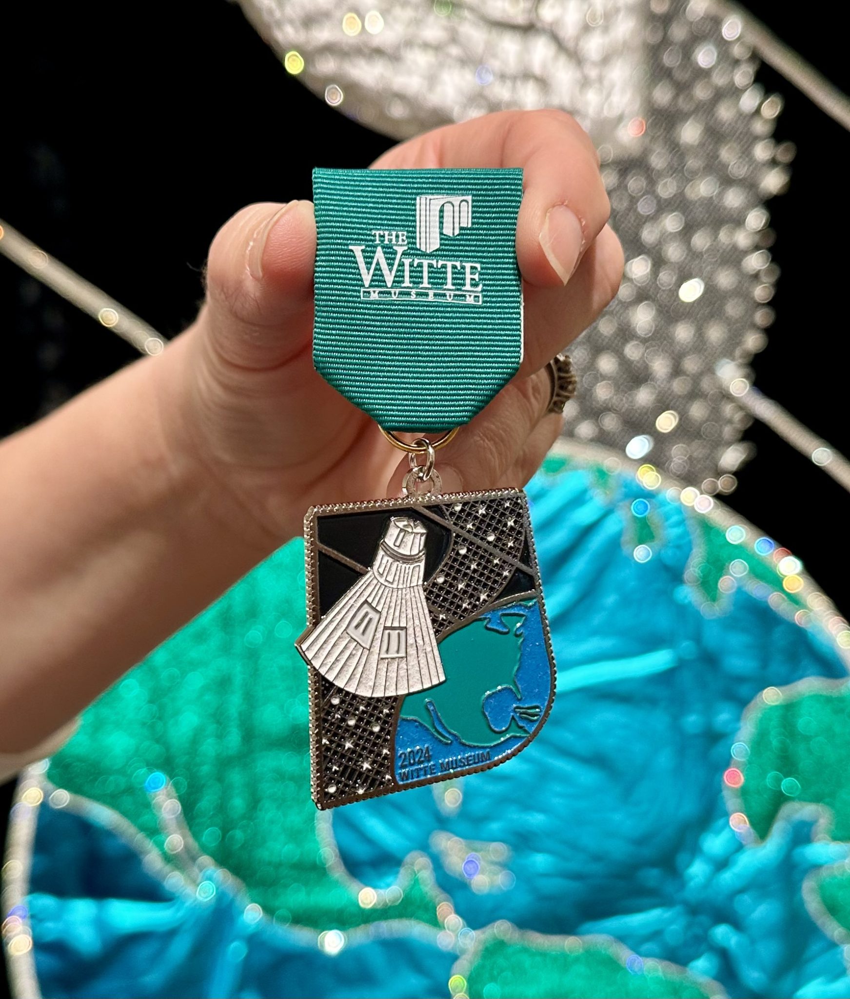 Black, white, teal and green Fiesta medal with space capsule and Earth